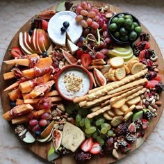 a wooden platter filled with cheese, fruit and crackers