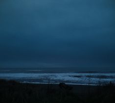 an empty beach at night with the ocean in the distance and dark clouds above it