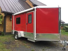 a red trailer is parked in front of a house with a metal roof and windows