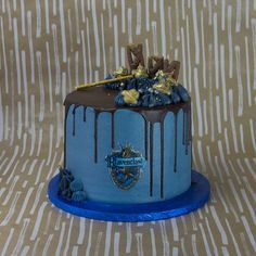 a blue cake with chocolate icing and gold decorations on top, sitting on a table