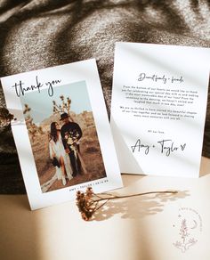 two wedding thank cards sitting on top of an open book next to a dried flower