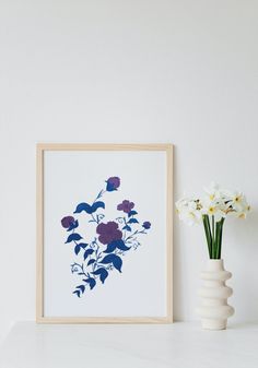 a vase with flowers sitting on top of a white table next to a framed photograph