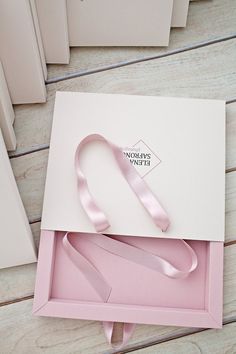 a pink ribbon in a white box on a wooden floor next to other boxes and papers