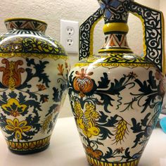 two large vases sitting on top of a table next to each other with designs painted on them