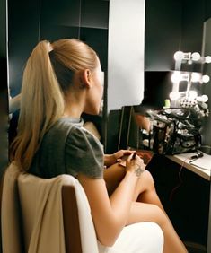 a woman sitting in front of a mirror looking at her hair and make - up