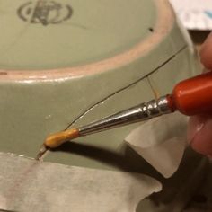 a person holding a paintbrush in their left hand and painting the inside of a bowl