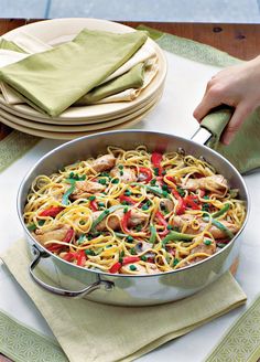 a pan filled with pasta and vegetables on top of a table next to place mats