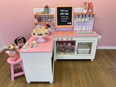 a toy kitchen with pink counter tops and wooden flooring next to a chalkboard on the wall