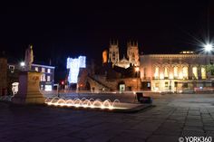 an illuminated fountain in the middle of a city square