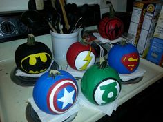 four painted pumpkins with batman and captain america designs on them sitting on a counter