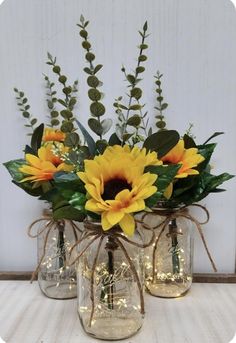 three mason jars filled with yellow flowers and greenery