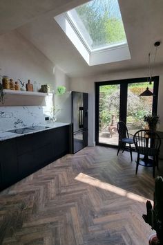 Dark wood herringbone flooring in a kitchen with black cabinets and  white marble topes, there is also  a black and white fridge and a table and chairs to create a dining area. Dark Wood Floors Kitchen, Dark Herringbone Floor, Wood Floors Kitchen, Vintage Chateau, Antique Wood Floors, Brown Laminate Flooring, Dark Brown Floor, Herringbone Floors, Direct Wood Flooring