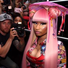 a woman with long pink hair is taking a selfie in front of a group of people