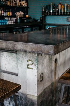 an empty bar with two stools and bottles on the wall in the back ground