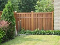 a wooden fence in front of a brick building with trees and shrubbery around it