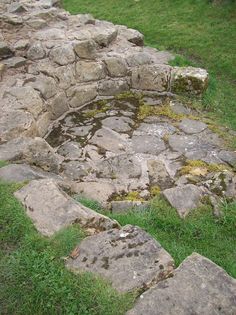 an old stone structure with moss growing on it's sides in the middle of a grassy area