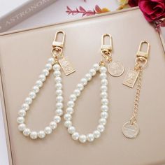 three pearls are attached to gold - plated keychains on a pink box