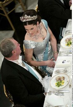 a man and woman sitting at a table in formal wear with plates on the table