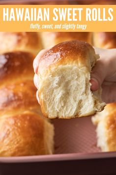 a person holding a piece of bread in front of a baking pan filled with rolls