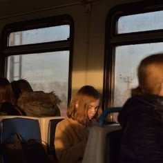 two people sitting on a bus looking at their cell phones while the other person looks down