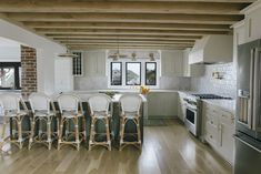 a kitchen filled with lots of white furniture and wooden beams over the counter top area