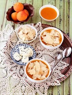 three bowls of food on a doily with spoons and oranges in the background