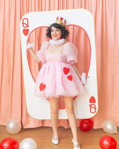 a woman in a pink dress standing next to a backdrop with balloons and hearts on it