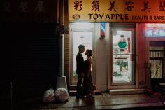 a man and woman standing in front of a store with the door open at night