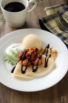 a white plate topped with food next to a cup of coffee on top of a wooden table