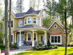 a yellow house in the middle of some trees and flowers on the grass with bushes around it