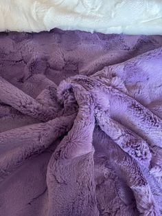 a purple blanket is laying on top of a white bed sheet that has been folded over