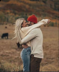 a man and woman embracing in the middle of an open field with cows behind them