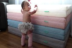 a baby girl standing next to several mattresses