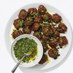 a white plate topped with meatballs next to a bowl of green pesto sauce