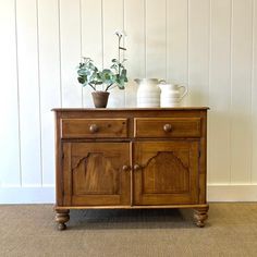 a wooden cabinet with two vases on top of it and one potted plant