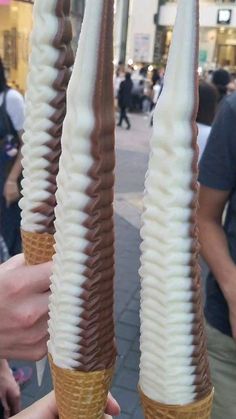 three ice cream cones with chocolate and white icing in their hands, on a city street