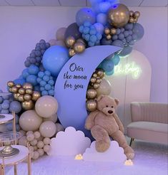 a teddy bear sitting in front of a balloon arch with balloons on it and a sign that says, over the moon for you