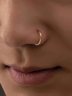 a woman wearing a nose piercing with a gold ring on it's nose and the end of her nose