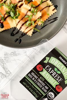 a black plate topped with pasta and sauce next to a carton of organic ravioli