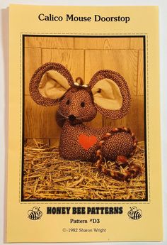 a stuffed mouse sitting on top of hay in front of a wooden wall with the words calico mouse doorstep