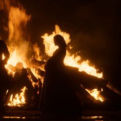 two people standing in front of a fire with flames coming out of the back ground