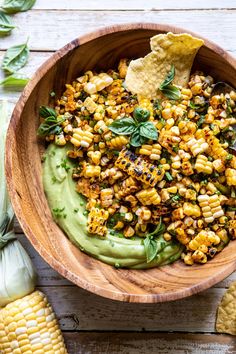 a wooden bowl filled with corn and guacamole next to corn on the cob