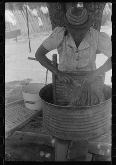 an old black and white photo of a person in a hat stirring something into a bucket