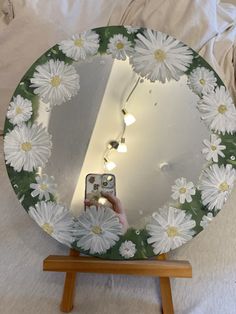 a hand holding a cell phone in front of a mirror with white flowers on it