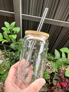 a hand holding a clear glass jar with pink flowers on it and a straw lid