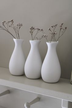 three white vases sitting on top of a shelf next to each other with flowers in them