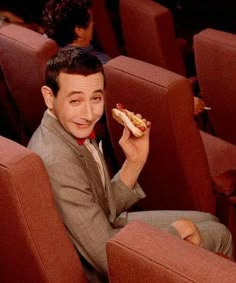 a young man sitting in a movie theater eating a hot dog