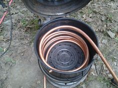 an open metal pot sitting on top of a grass covered ground next to a hose