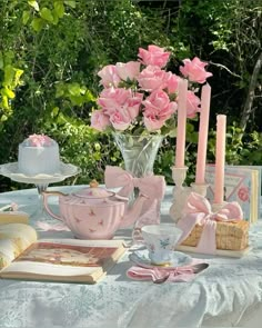 a table topped with pink roses and teacups next to an open book on top of a white table cloth