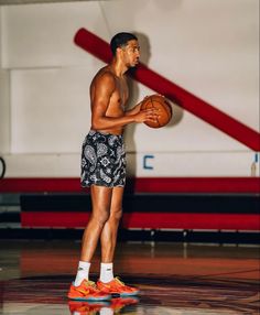 a young man holding a basketball on top of a gym floor in front of a red and white wall